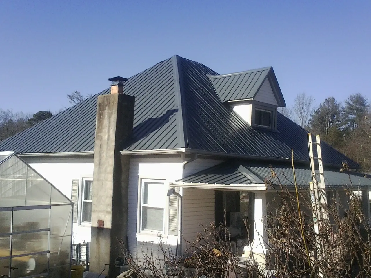 Dark blue standing seam metal roof on a white farmhouse with dormer — Slate & Tile Roof Repair by Roofing Brothers in Cooperstown