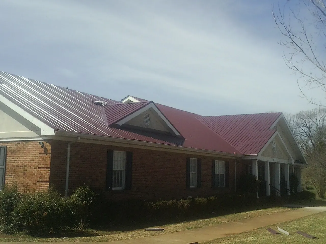 Red metal roof with gabled entries on a long brick building, from a Hail Damage Roof Repair job in Cooperstown