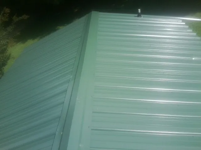 New green metal panels meeting at the ridge of a roof — Flat Roof Repair work by our crew in Cooperstown