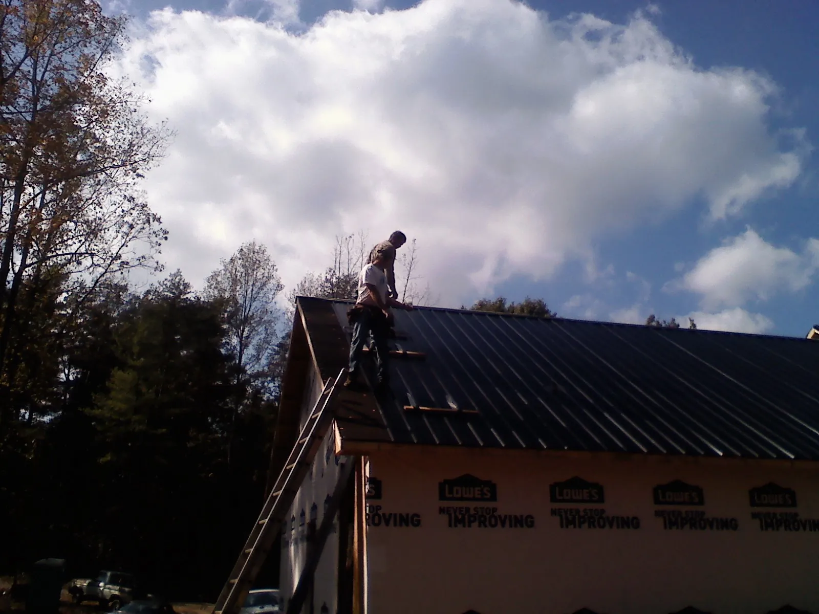 Roofer fastening dark metal panels high against a cloudy sky, from a Roof Inspection job in Cooperstown