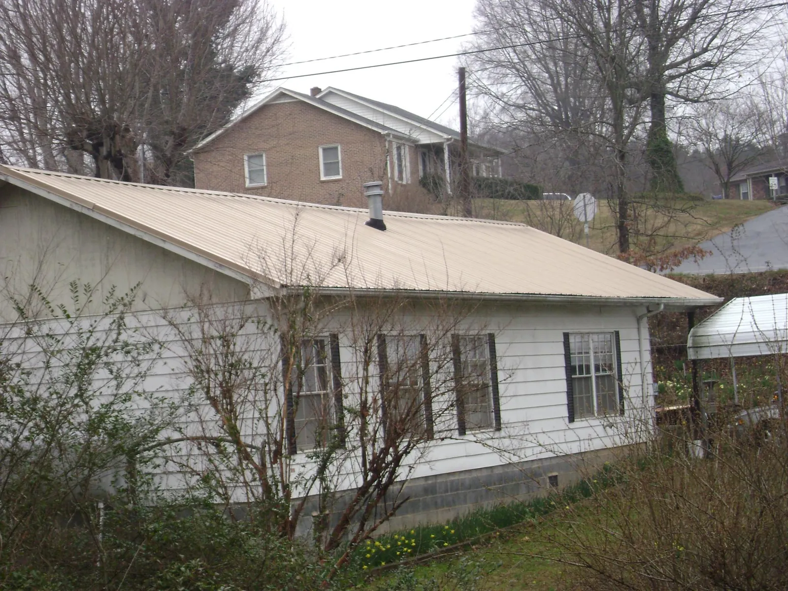 Tan metal roof on a white sided house set into a hillside — Commercial Roofing by Roofing Brothers in Cooperstown