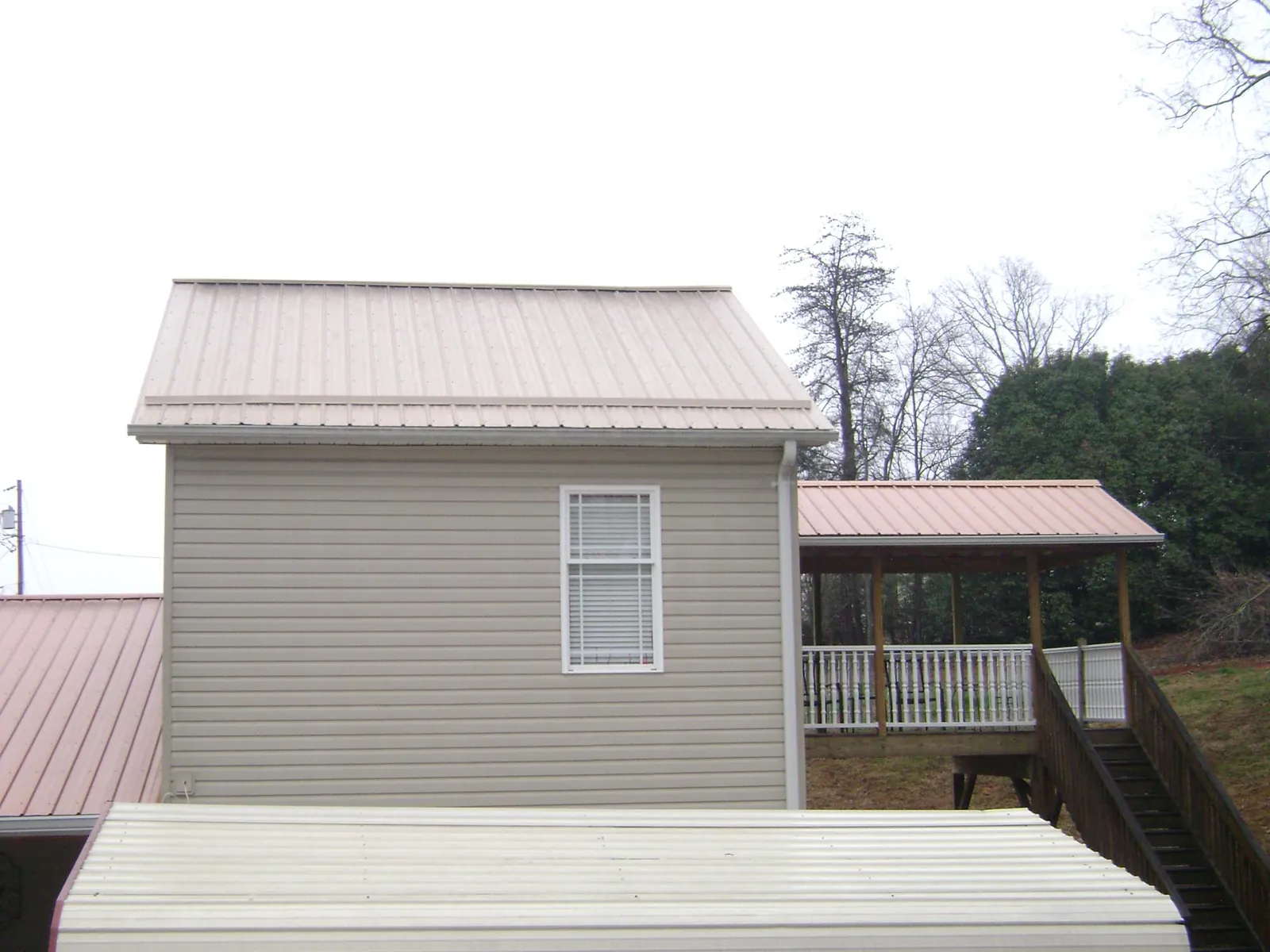 Tan metal roofs on a two story addition and attached porch, from a Roof Replacement job in Cooperstown